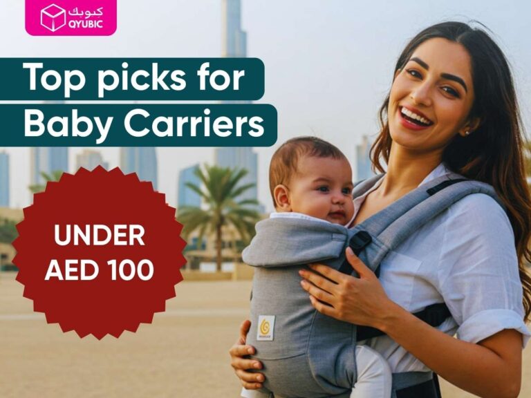 Smiling mother wearing a grey baby carrier on a Dubai beach, text ‘Top picks for Baby Carriers – Under AED 100,’ and Qyubic logo