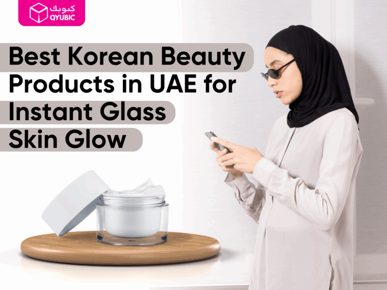 A Muslim woman in a hijab uses her phone while standing indoors, next to a cosmetic jar on a wooden platform. The image promotes “Best Korean Beauty Products in UAE for Instant Glass Skin Glow” by QYUBIC, a discount and coupon platform.