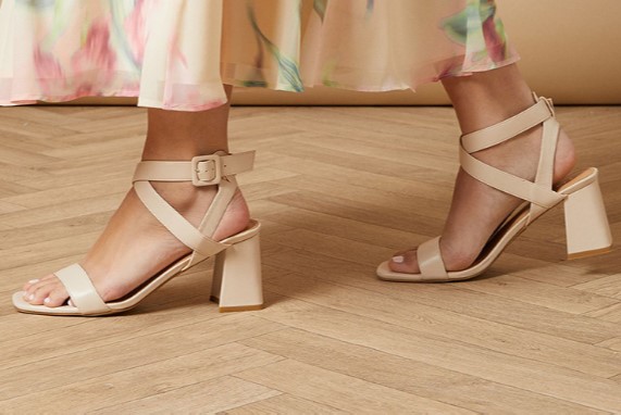 An image of walking feet with a beautiful, casual pair of heeled sandals with a steady height for flat feet.