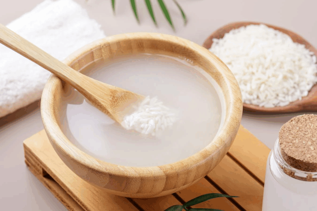 Bowl of rice water with wooden spoon, showcasing a traditional Korean beauty ingredient known for brightening and hydrating, featured in top Noon Korean skincare products.