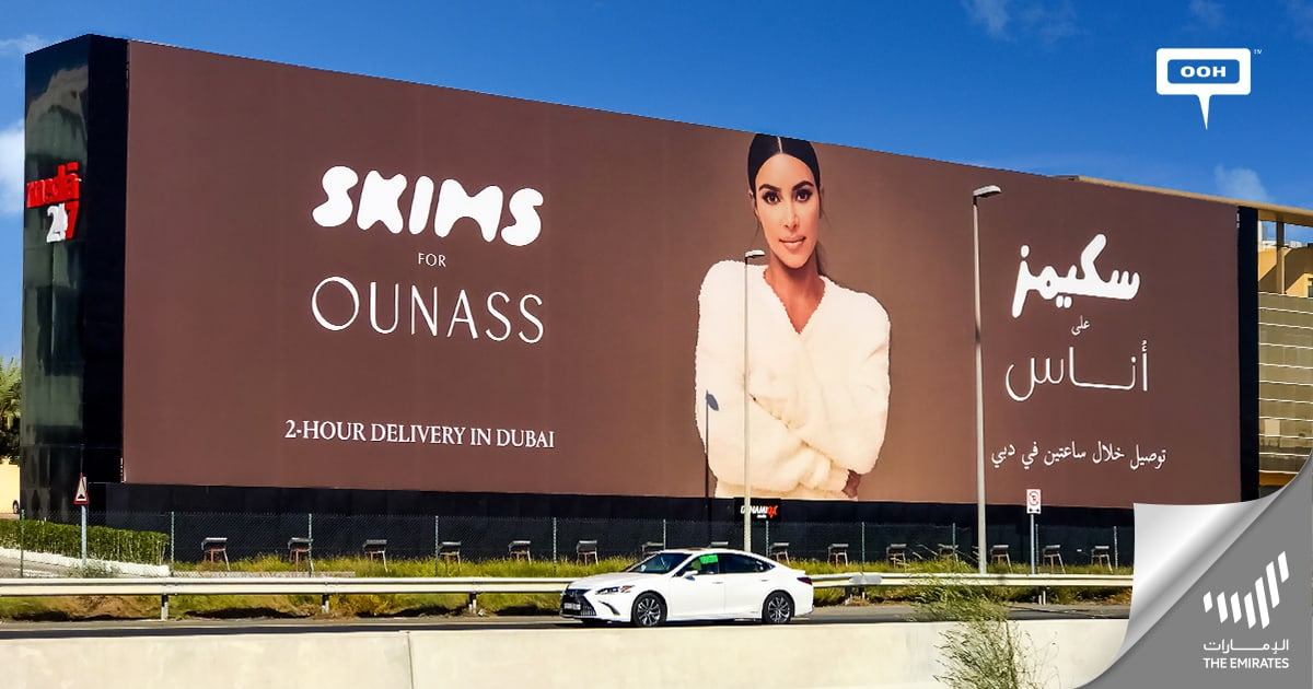 A large outdoor advertisement for SKIMS by Ounass, featuring a model in a cream-colored outfit. The billboard highlights a '2-hour delivery in Dubai' service with English and Arabic text.